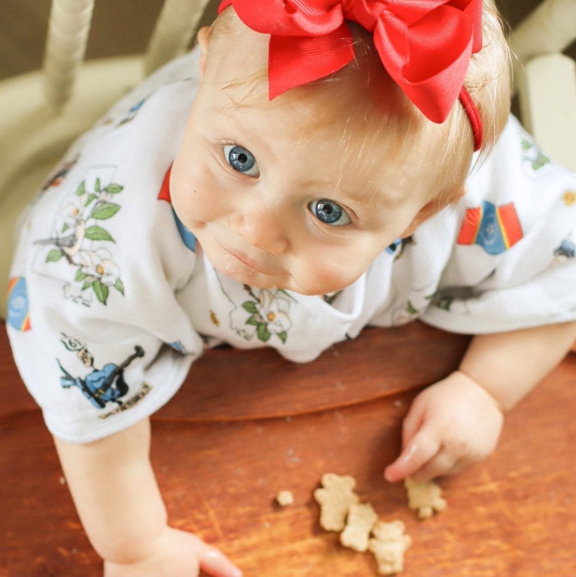 The same little crawler looks up mid reach on the wood floor in her Mississippi burp cloth and bib combo.