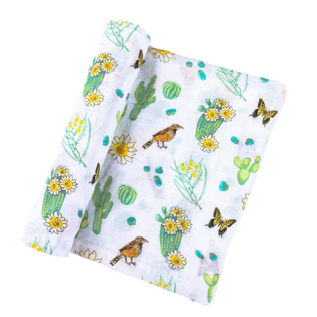 The Cactus Blossom muslin swaddle blanket folded into soft waves, prickly pears and desert birds.