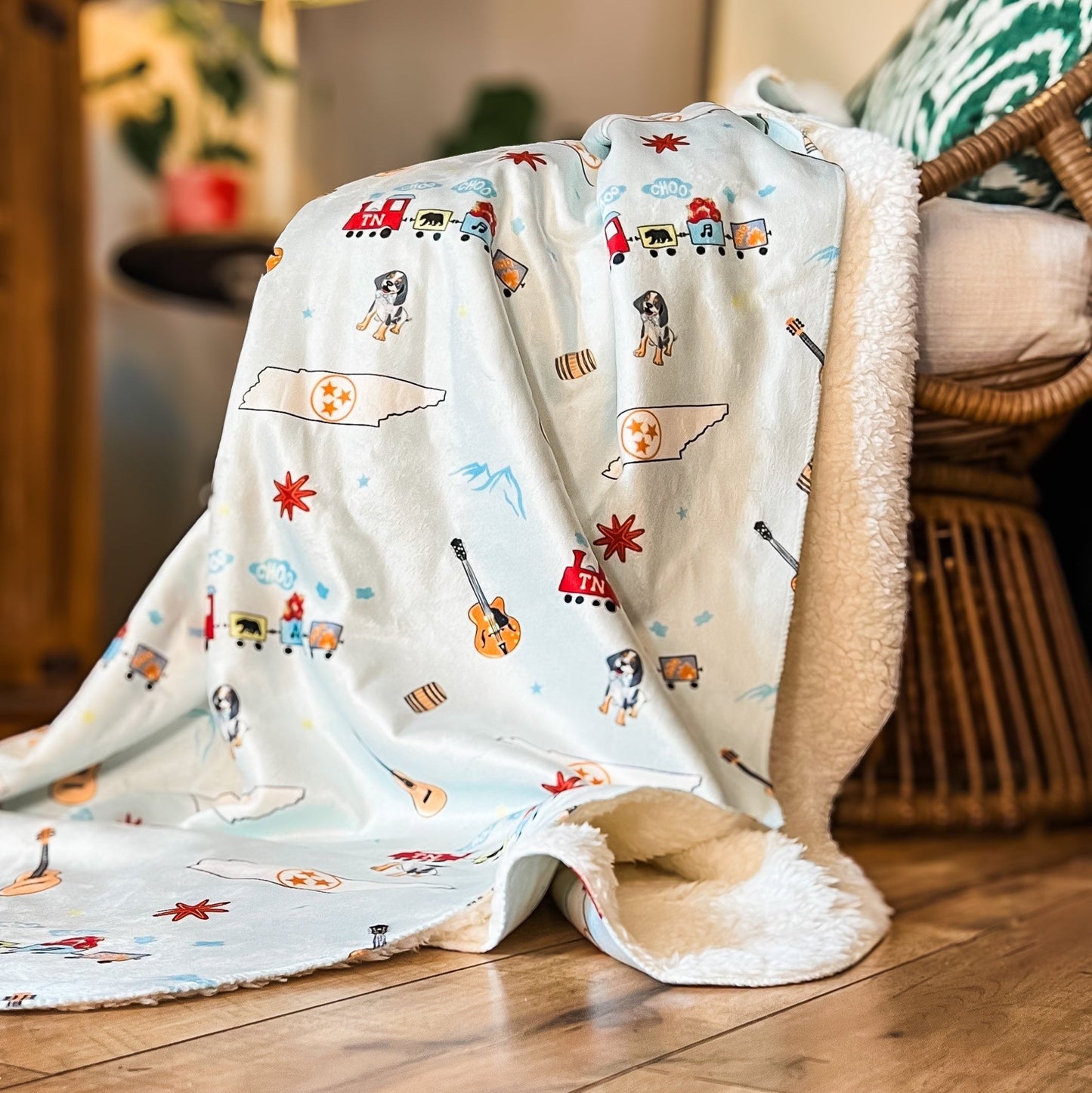 The Tennessee Blue plush throw blanket spills over a woven chair in a warm lit room at home.