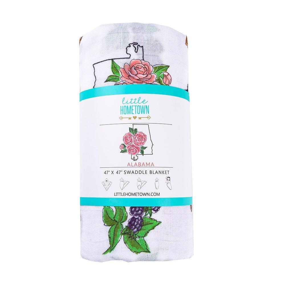The Alabama Floral muslin swaddle blanket rolled and banded, camellias winding all the way around.