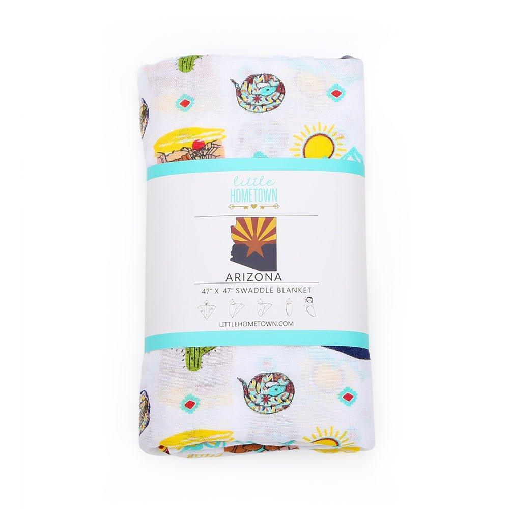 The Arizona muslin swaddle blanket folded and banded, cacti and desert sun peeking through.
