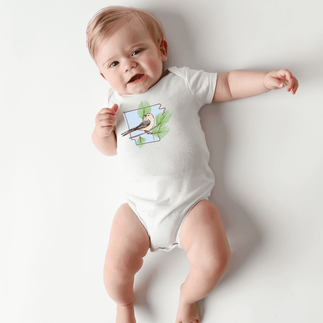 A happy baby stretches out laughing on a white backdrop in the Arkansas Pine baby onesie.