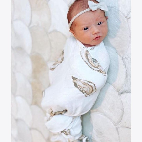 White muslin swaddle blanket with playful oyster illustrations and the text "Aw Shucks!" in blue script.