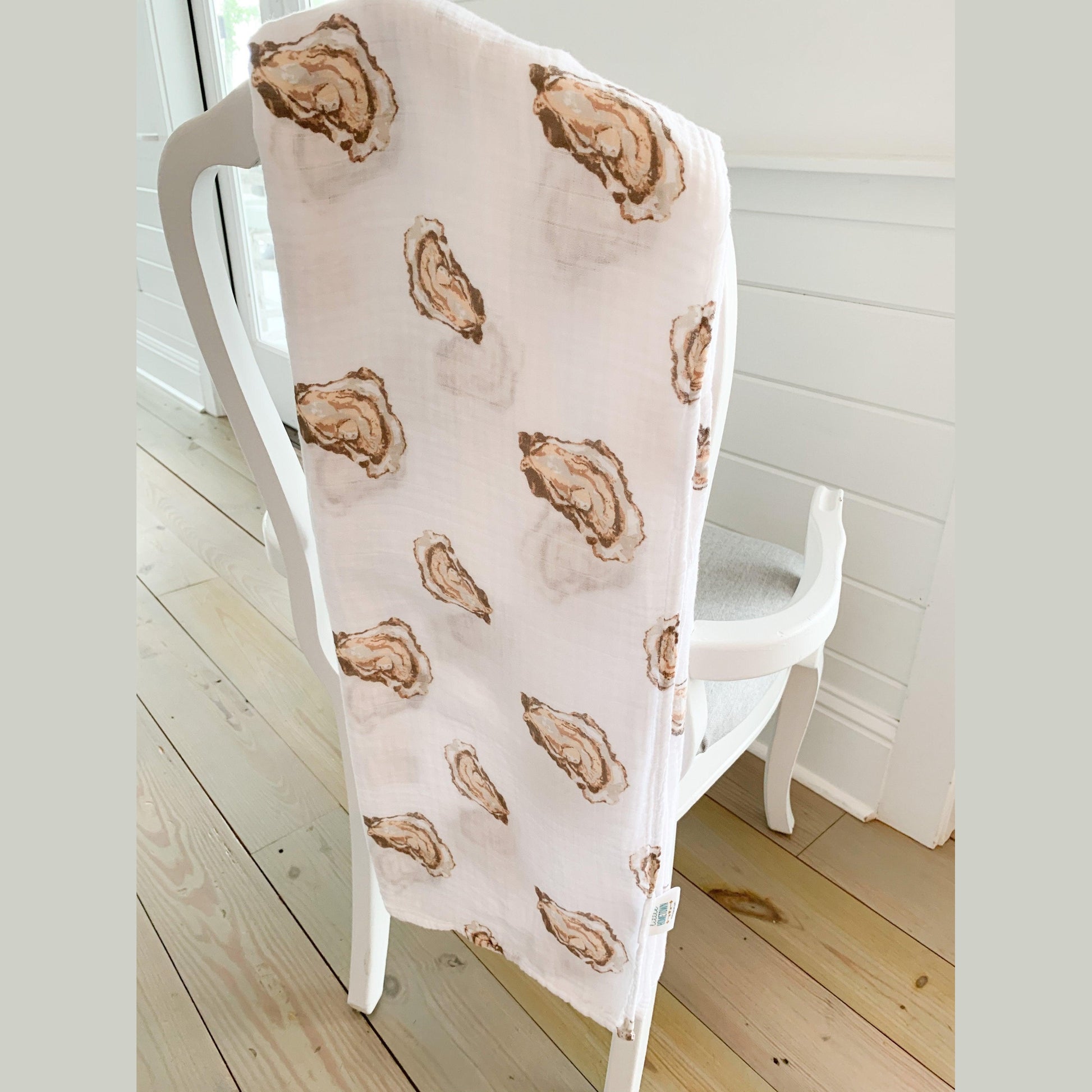White muslin swaddle blanket with playful oyster illustrations and the text "Aw Shucks!" in blue script.