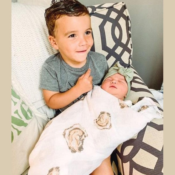 White muslin swaddle blanket with playful oyster illustrations and the text "Aw Shucks!" in blue script.