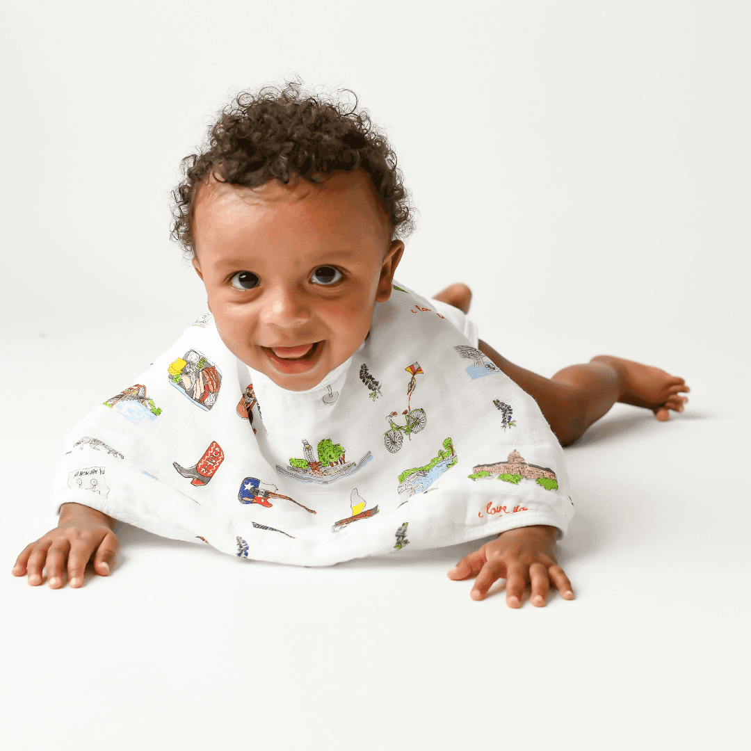 A baby pushes up onto his hands in the Austin, Texas burp cloth and bib combo, mid crawl and full of purpose.
