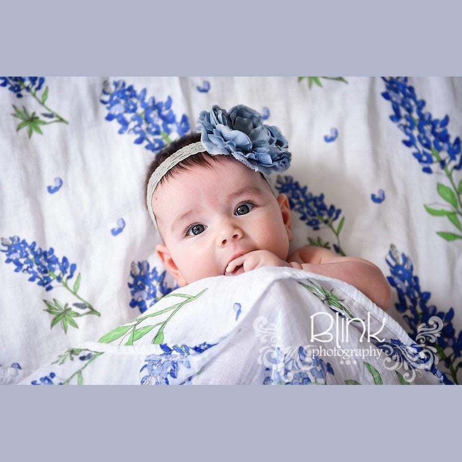 White muslin swaddle blanket with bluebonnet floral pattern, neatly folded on a white background.