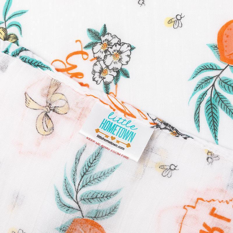Baby swaddled in a white muslin blanket with "Georgia Girl" text and peach illustrations, lying on a soft surface.