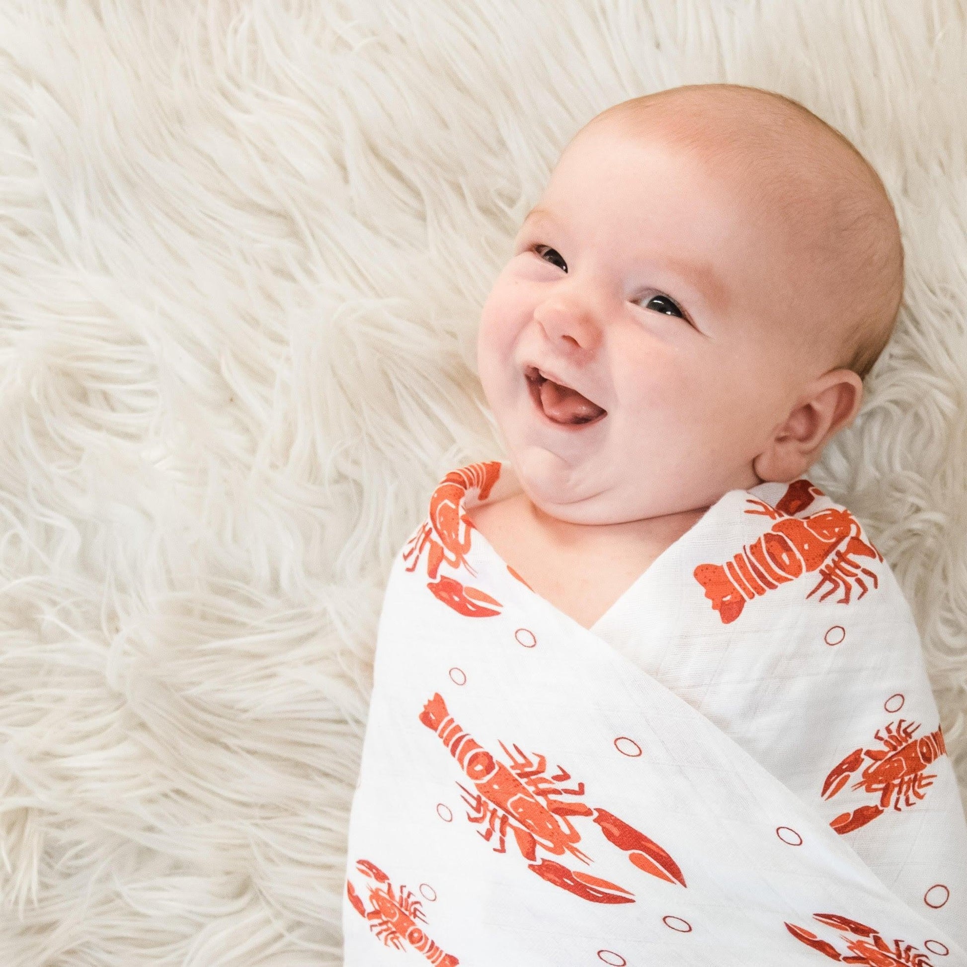 White muslin baby swaddle blanket with playful blue and green fish pattern, folded neatly on a white background.