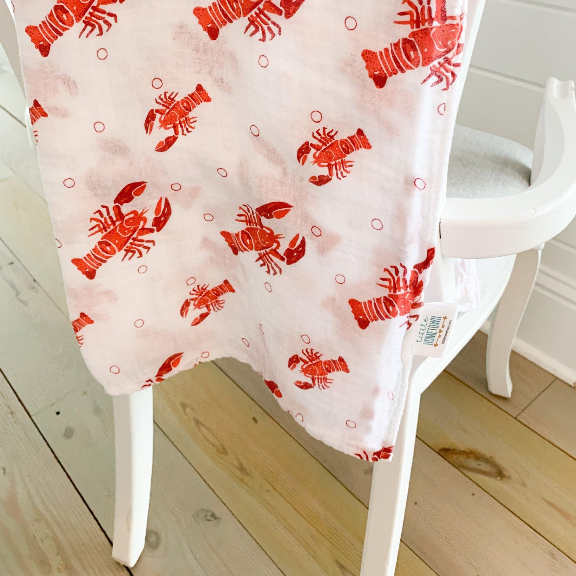 White muslin baby swaddle blanket with playful blue and green fish pattern, folded neatly on a white background.