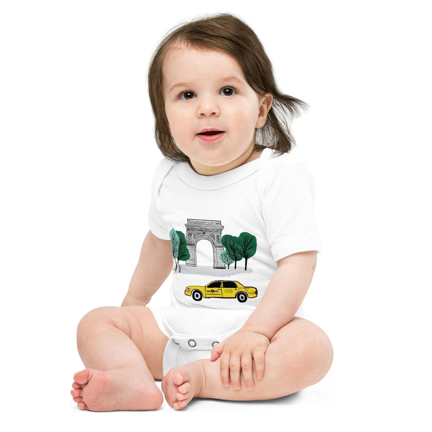 A smiling toddler sits cross legged in the New York City Washington Square Park baby onesie.