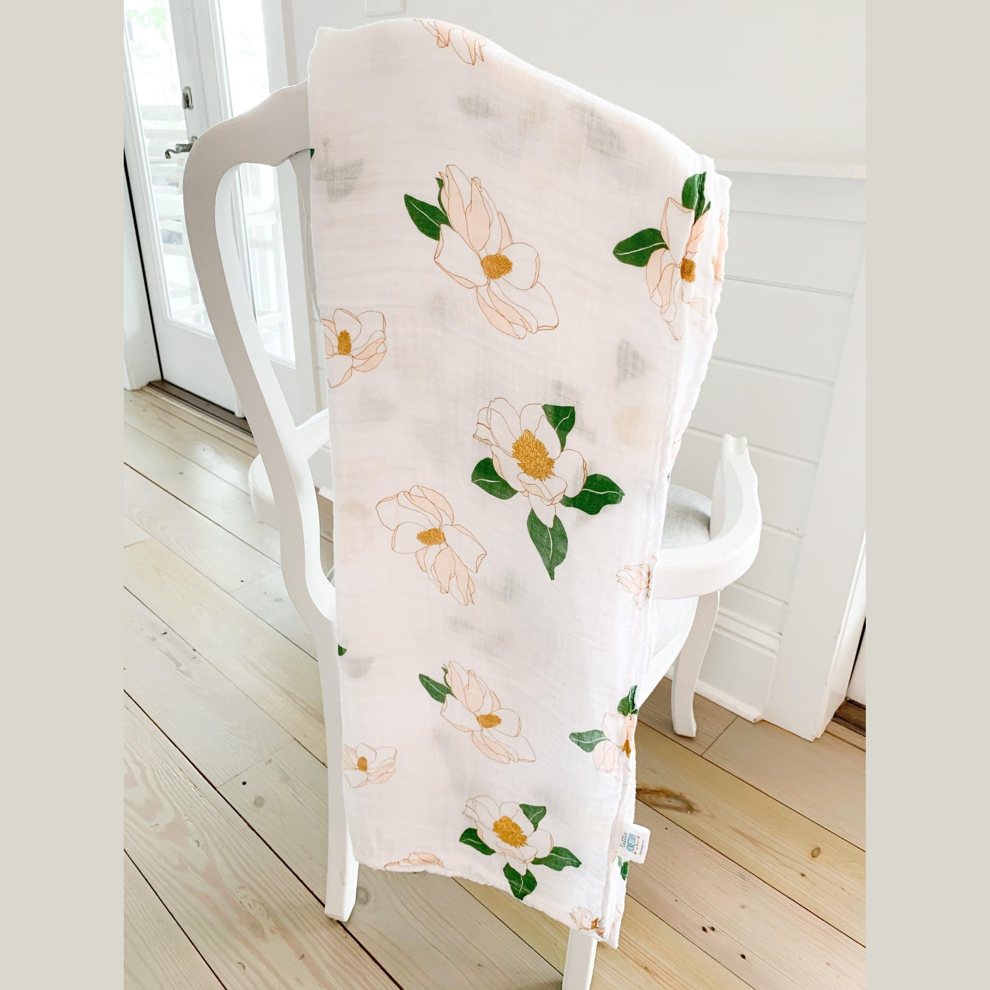 Soft muslin baby swaddle blanket with delicate Southern Magnolia floral print in pastel colors on a white background.