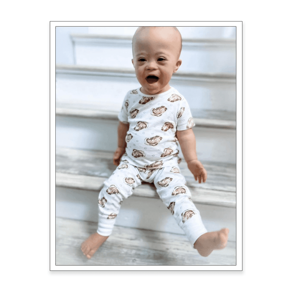 Woman in oyster-patterned pajamas, smiling and holding a mug, standing in a cozy, well-lit kitchen.