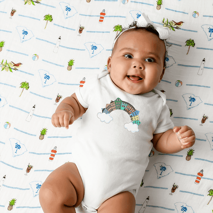 White baby onesie with colorful "Charleston Rainbow Row" text and pastel houses illustration.