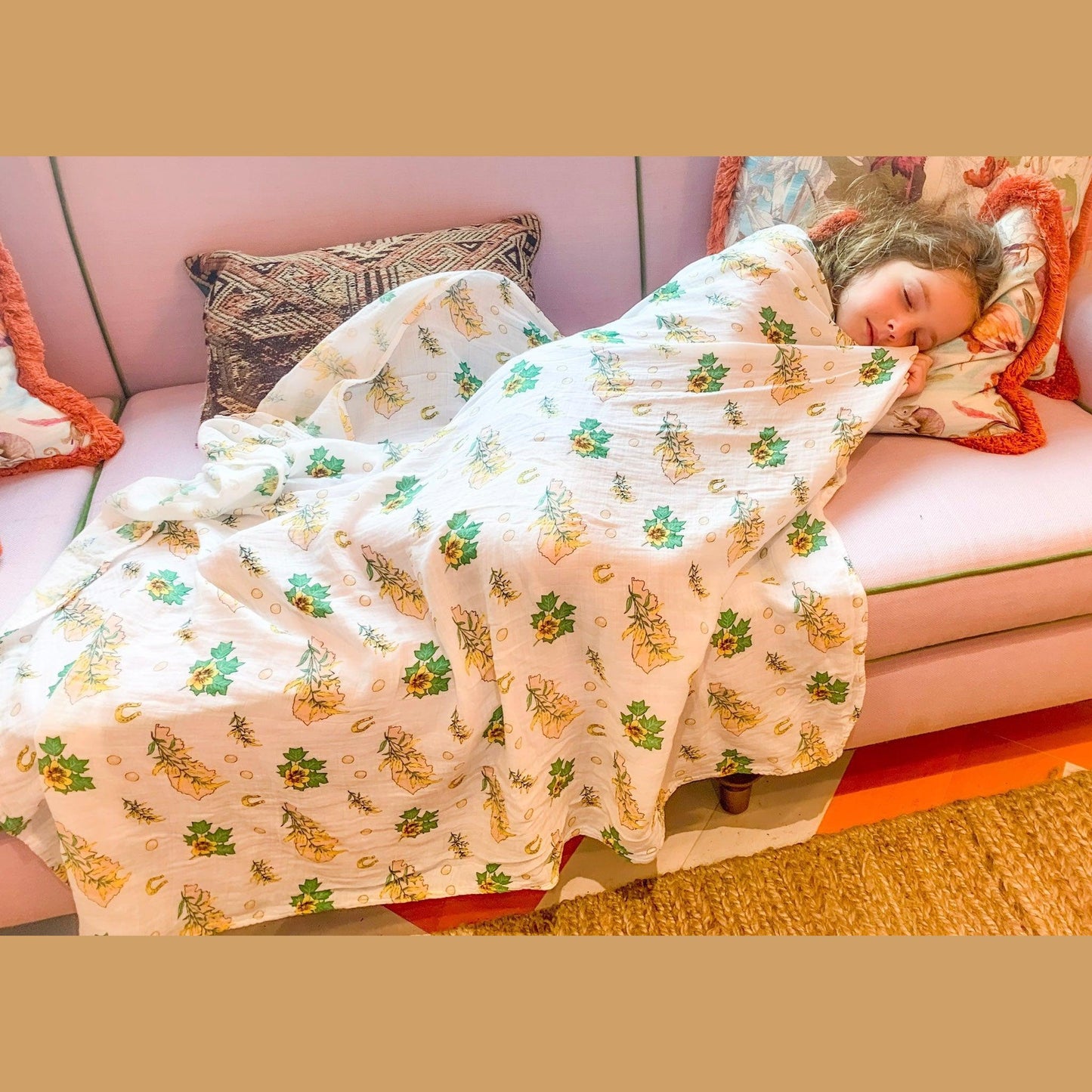 A baby rests in soft golden light with the Kentucky floral muslin swaddle blanket drawn up to her chin.