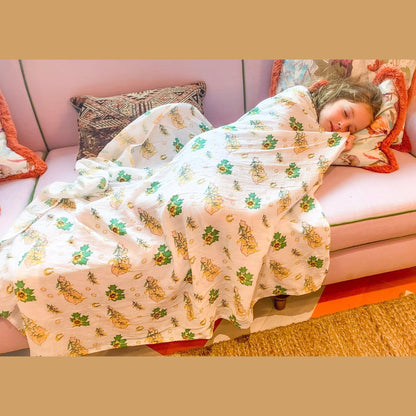 A baby rests in soft golden light with the Kentucky floral muslin swaddle blanket drawn up to her chin.