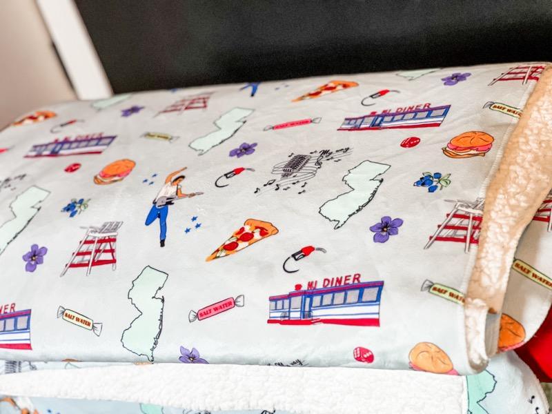 Cozy New Jersey-themed folded plush blanket featuring state map, landmarks, foods, and cultural icons