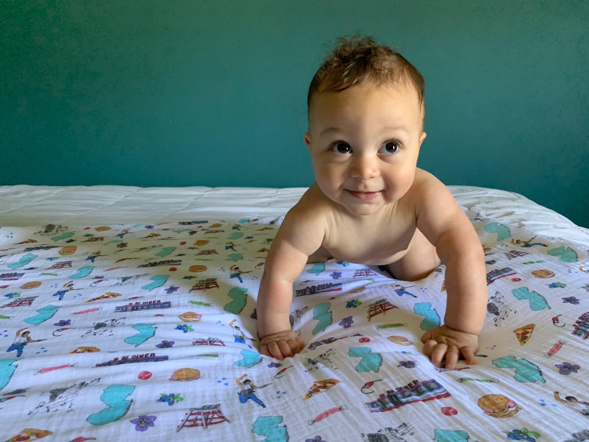 A smiling baby crawling on a cozy New Jersey-themed swaddle bundle featuring state map,  landmarks, foods, and cultural icons