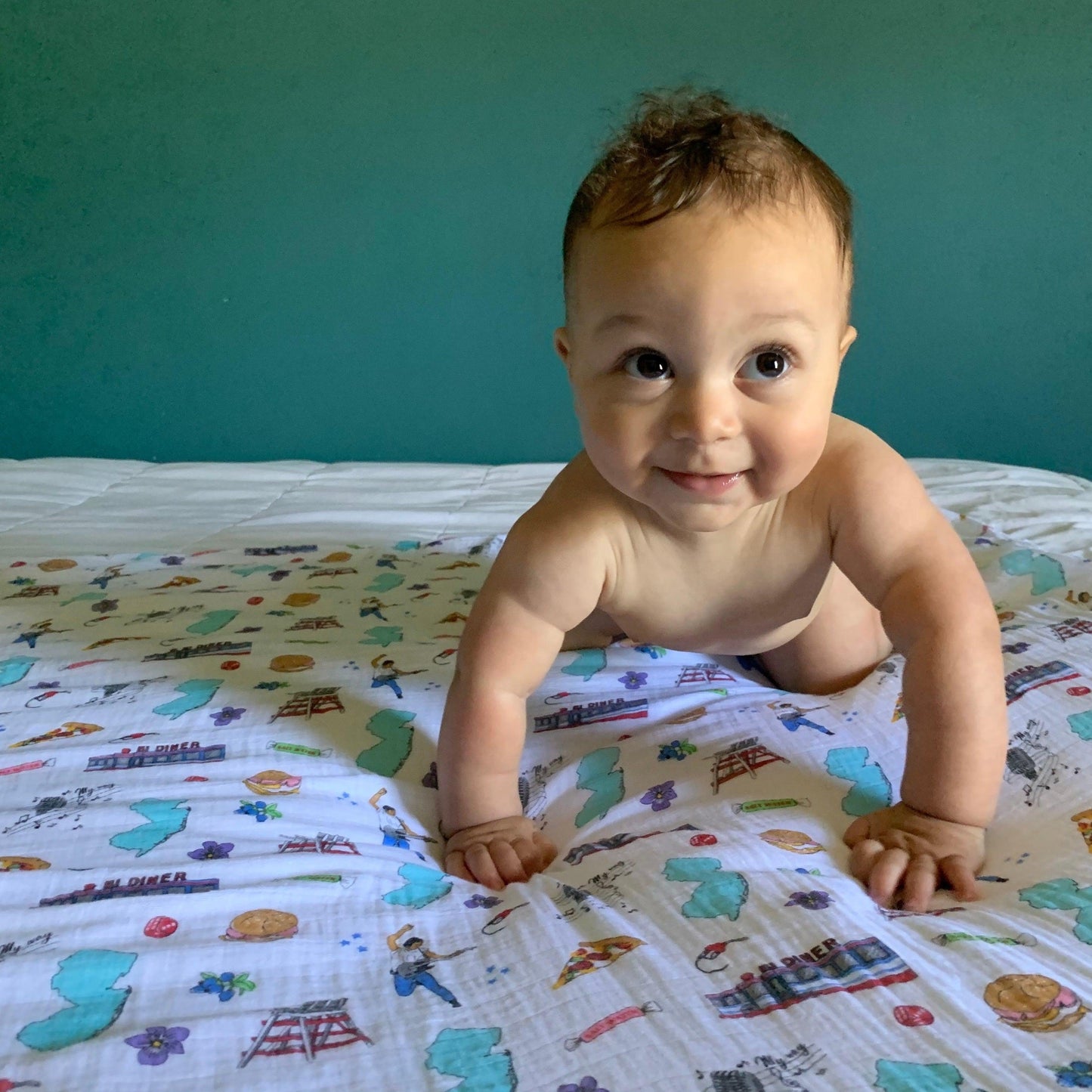 A smiling baby crawling on a cozy New Jersey-themed swaddle bundle featuring state map,  landmarks, foods, and cultural icons