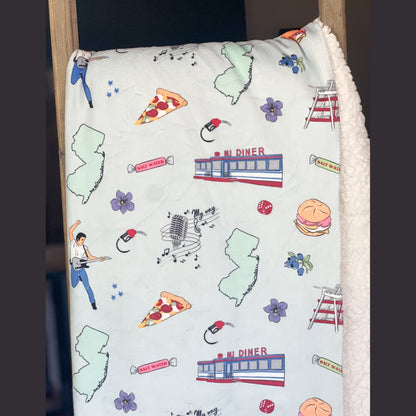 New Jersey-themed plush throw blanket, 60x80 inches, featuring a detailed map with landmarks, a rock star with his guitar, pizza, a diner, a gas pump, musical notes, flowers, and vibrant colors.