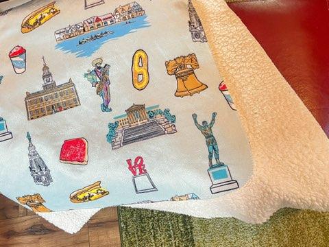 Philadelphia plush throw blanket, 60x80 inches, featuring many elements of Philadelphia like Rocky, Liberty Bell, Jason Kelce as a Mummer, water ice, cheesesteak and other items and colors in a cozy, soft fabric.
