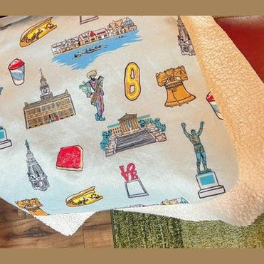 Philadelphia plush throw blanket, 60x80 inches, featuring many elements of Philadelphia like Rocky, Liberty Bell, Jason Kelce as a Mummer, water ice, cheesesteak and other items and colors in a cozy, soft fabric.