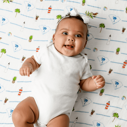 White muslin swaddle blanket with a colorful map of South Carolina, featuring landmarks, animals, and state symbols.