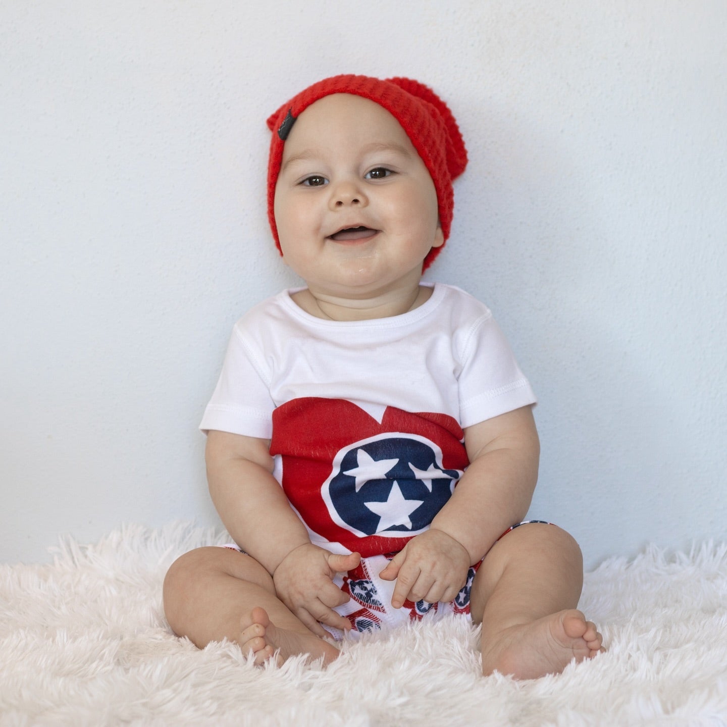 White baby onesie with a red heart and "Tennessee" text, displayed on a wooden background.