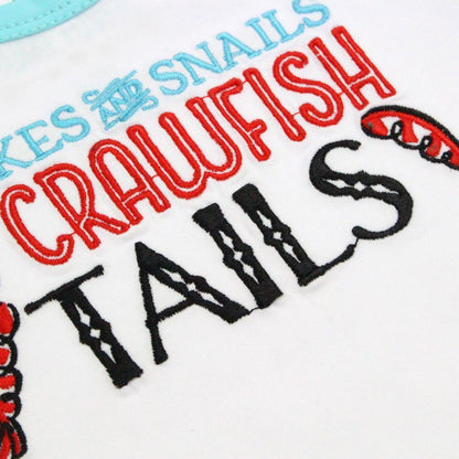 White baby onesie with "Snakes and Snails and Crawfish Tails" text, featuring colorful crawfish and snail illustrations.