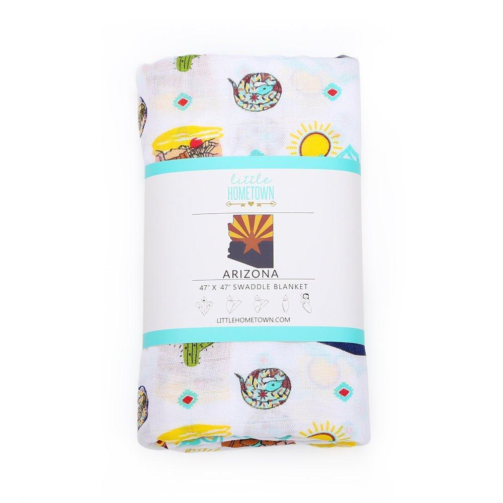 White muslin swaddle blanket with a colorful Arizona-themed print featuring cacti, mountains, and desert animals.