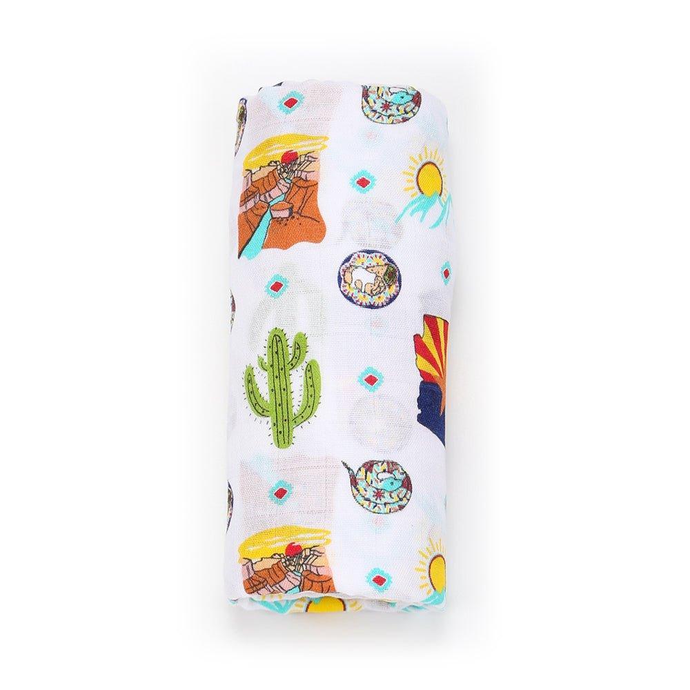 White muslin swaddle blanket with colorful Arizona-themed illustrations, including cacti, mountains, and desert animals.