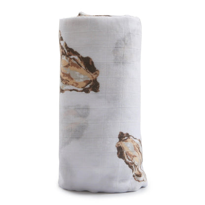 White muslin swaddle blanket with playful oyster illustrations and the text "Aw Shucks!" in blue.