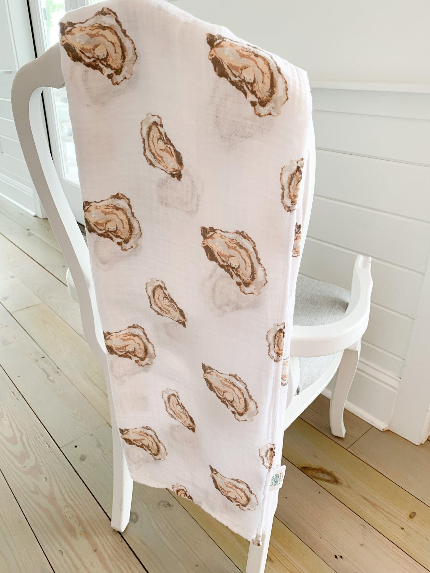 White muslin swaddle blanket with playful oyster illustrations and the text "Aw Shucks!" in blue script.