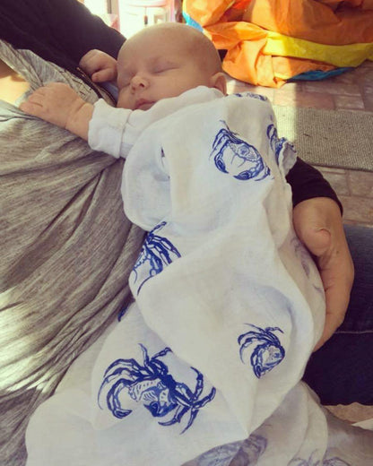 White muslin swaddle blanket with blue crab illustrations, featuring detailed claws and shells, on a white background.