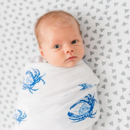 White muslin swaddle blanket with blue crab illustrations, perfect for a coastal-themed nursery.