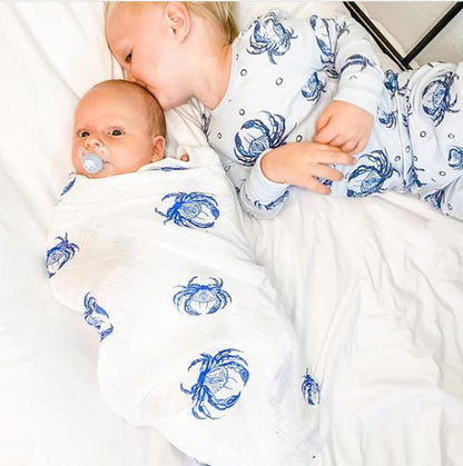 White muslin swaddle blanket with blue crab illustrations, folded neatly on a white background.