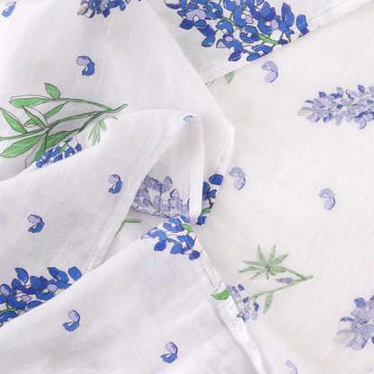 White muslin swaddle blanket with bluebonnet flower pattern, neatly folded on a white background.