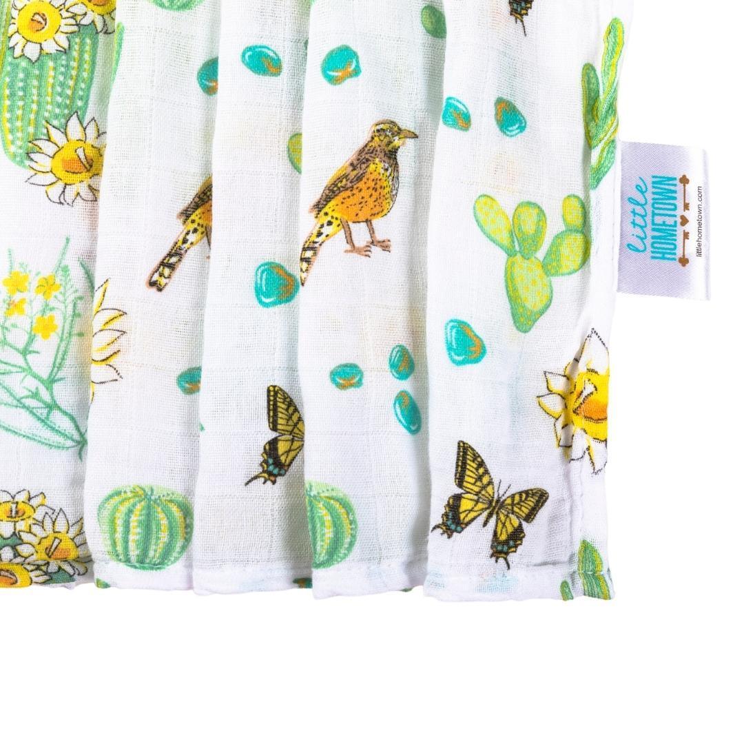 Soft muslin swaddle blanket with a vibrant cactus blossom print, featuring pink flowers and green cacti.