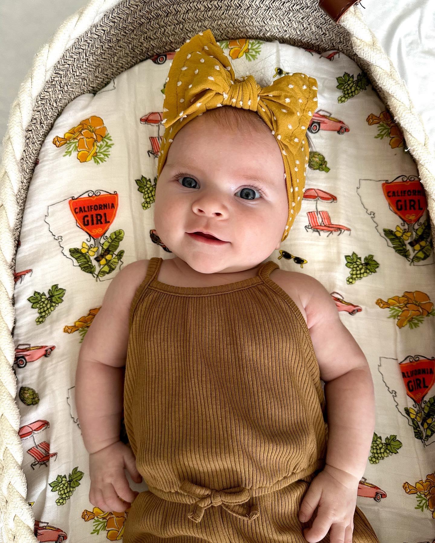 Baby girl wrapped in a soft, white muslin swaddle blanket with "California" and colorful icons printed on it.