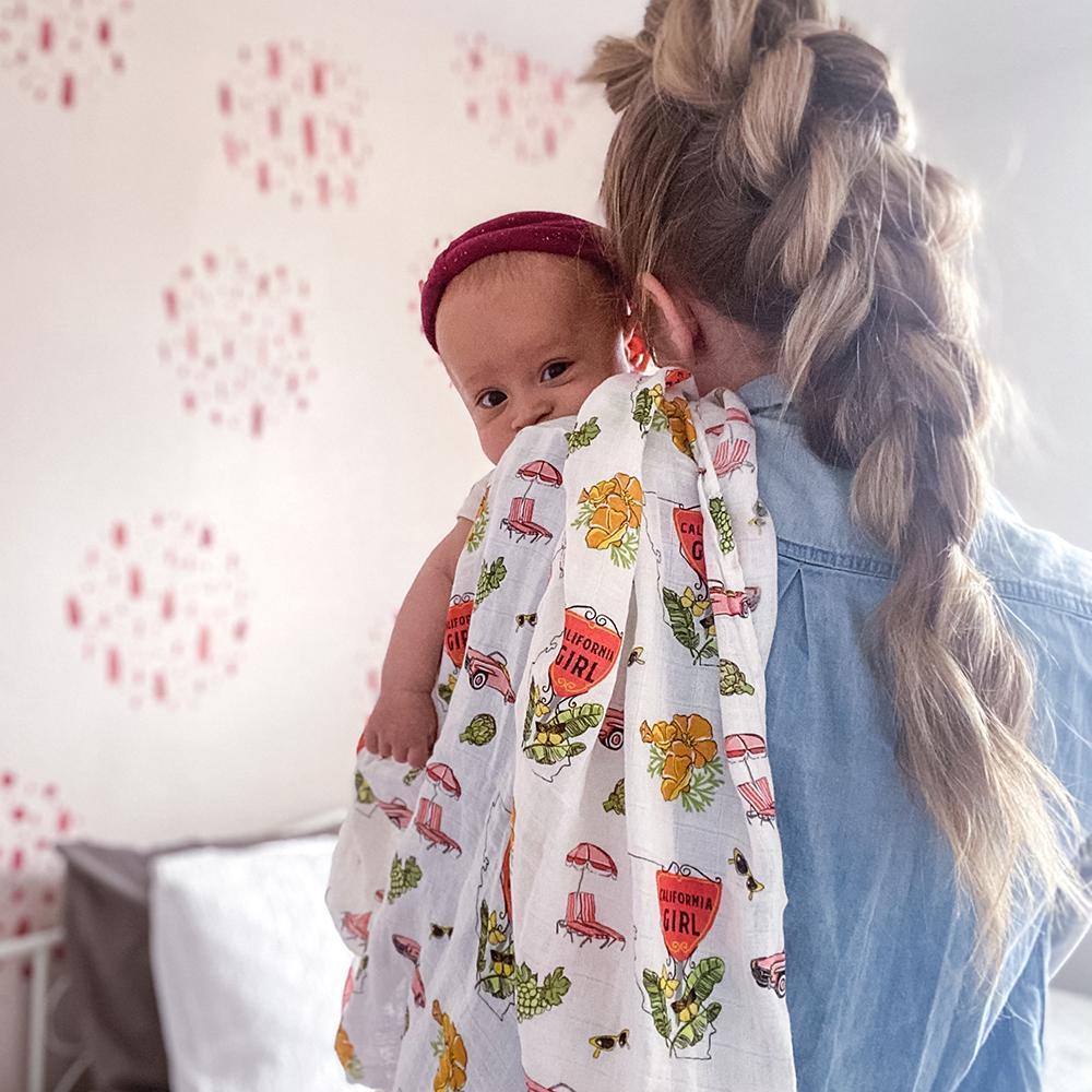 Baby girl muslin swaddle blanket with California-themed illustrations, including palm trees, surfboards, and bears.