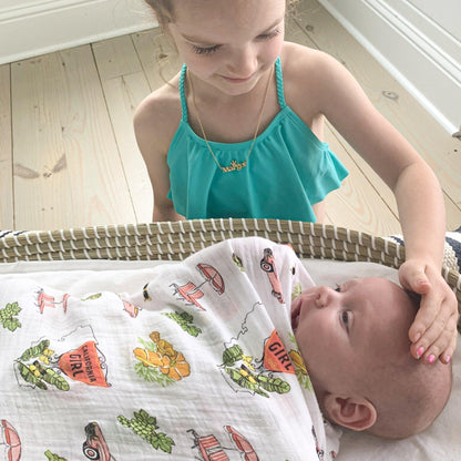 White muslin swaddle blanket with pink California-themed illustrations, including palm trees, surfboards, and landmarks.