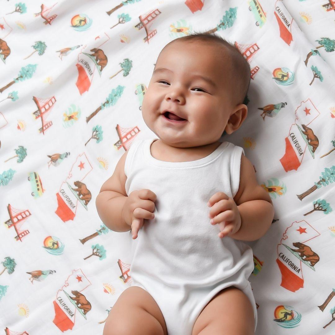 White muslin swaddle blanket with California-themed illustrations, including palm trees, surfboards, and bears.