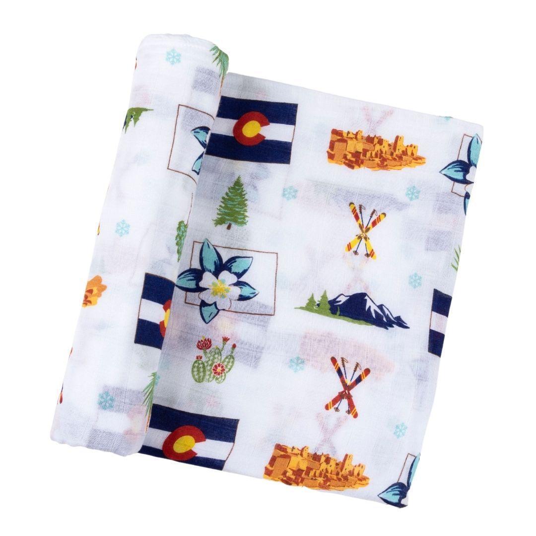 White muslin swaddle blanket with colorful Colorado-themed illustrations, including mountains, trees, and wildlife.