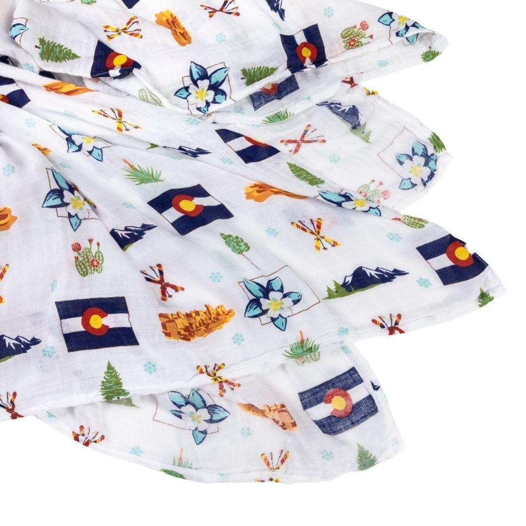 White muslin swaddle blanket with colorful Colorado-themed illustrations, including mountains, bears, and trees.