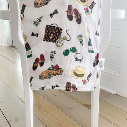 Baby swaddle blanket with a playful pattern of bow ties, mustaches, and glasses on a white background.