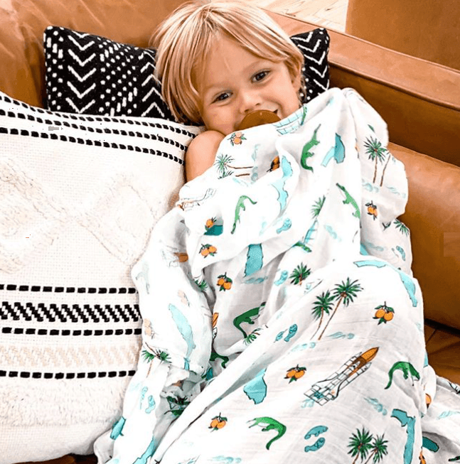 White muslin swaddle blanket with colorful Florida-themed illustrations, including oranges, flamingos, and palm trees.