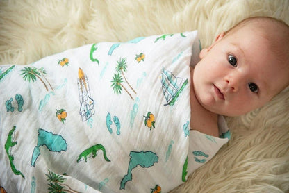 White muslin swaddle blanket with colorful Florida-themed illustrations, including oranges, flamingos, and palm trees.