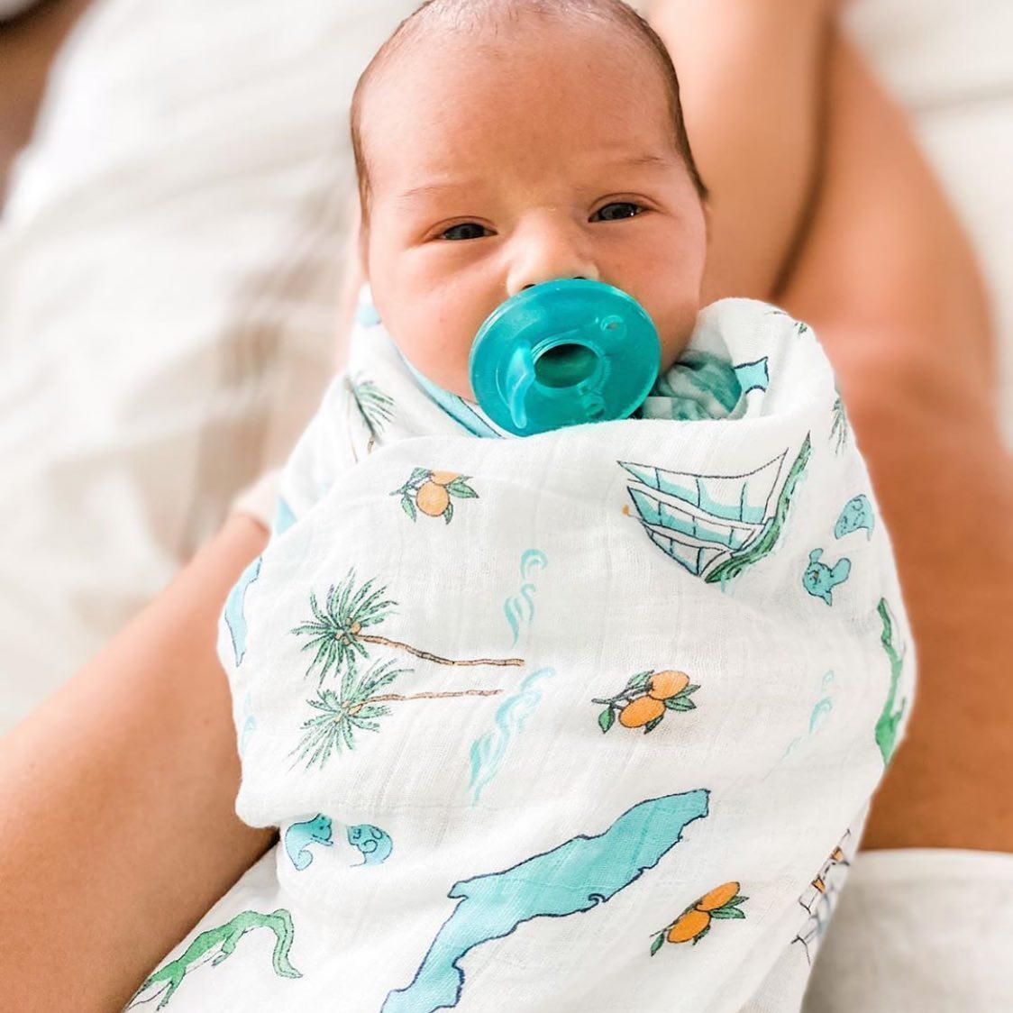 Florida-themed baby muslin swaddle blanket with colorful illustrations of palm trees, flamingos, and oranges.