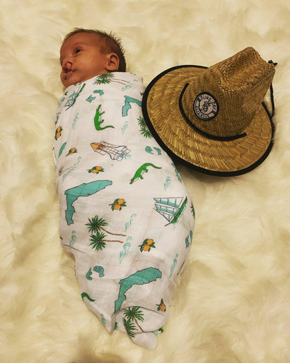 Florida-themed baby muslin swaddle blanket with colorful illustrations of palm trees, flamingos, and oranges.