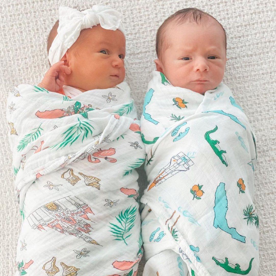 Florida-themed baby muslin swaddle blanket with colorful illustrations of palm trees, flamingos, and oranges.